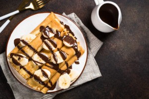 Plate of crepes with sliced bananas and chocolate drizzle