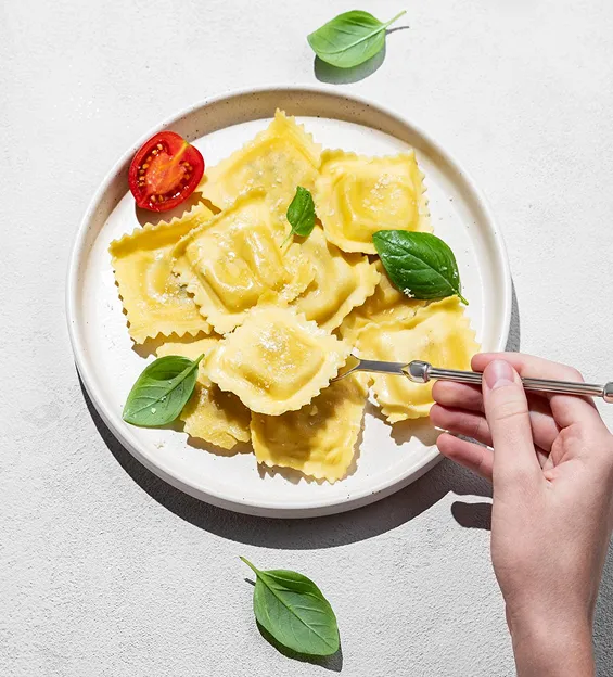 Hand picking ravioli from a plate garnished with basil and cherry tomato