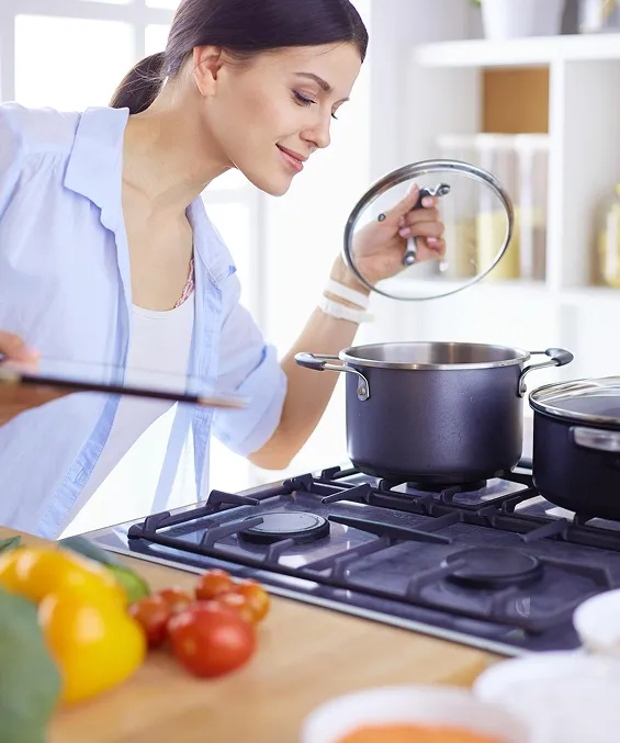 Woman checking pot on gas stove while cooking