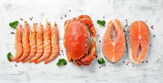 Fresh seafood including shrimp, crab and salmon steaks on white surface