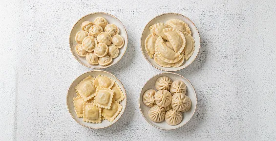 Four plates of assorted dumplings varieties on white background